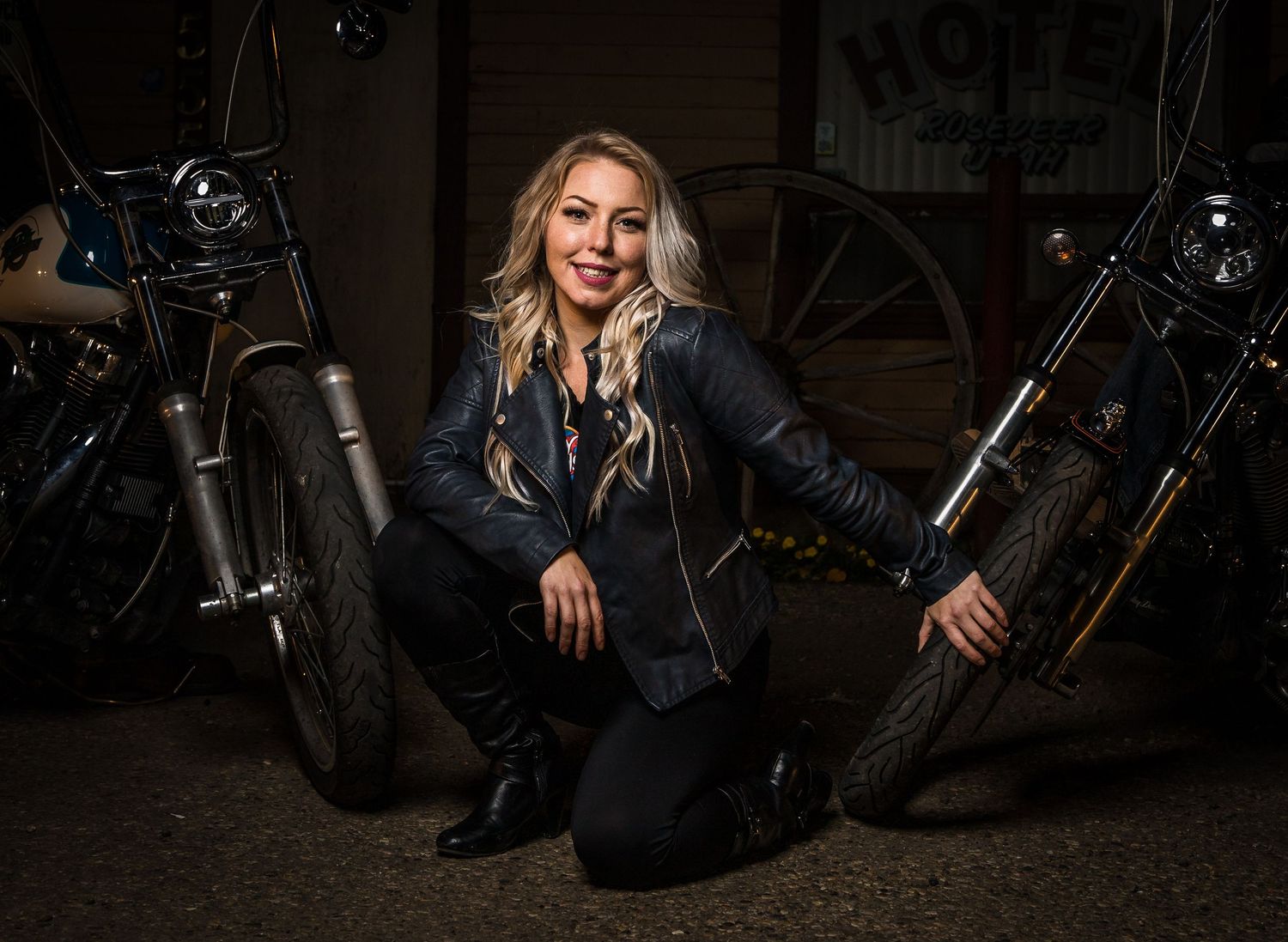 Dark moody portrait of someone posing between motorcycles wearing black leather.