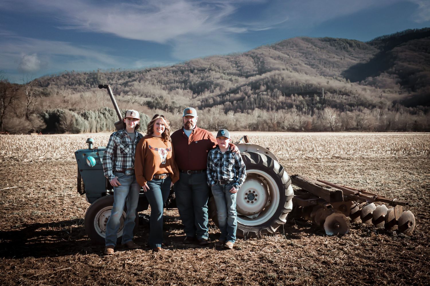 Group of farmers standing beside a vintage tractor in a winter field with mountains in background.