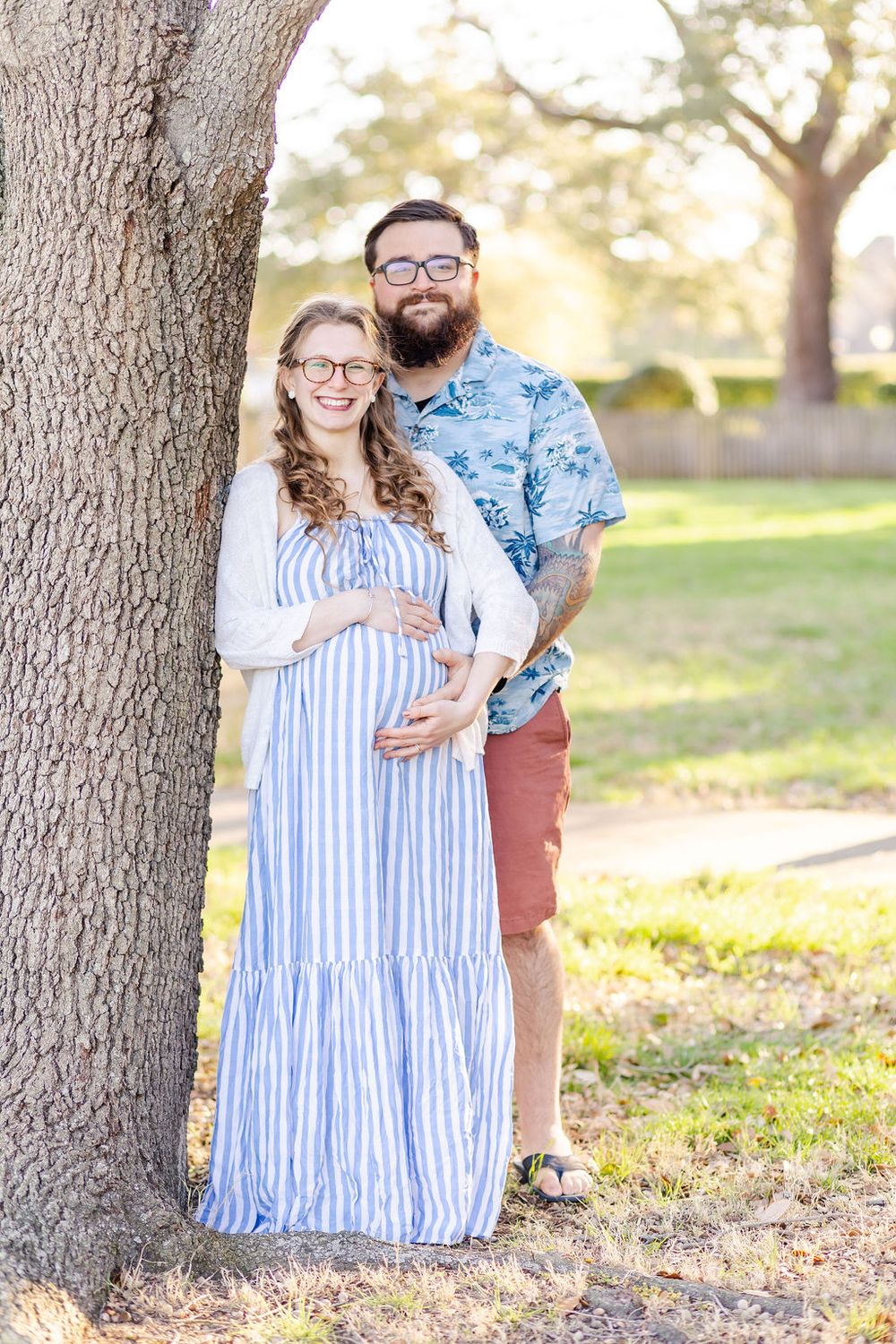 Couple poses together under large tree in outdoor maternity photoshoot.