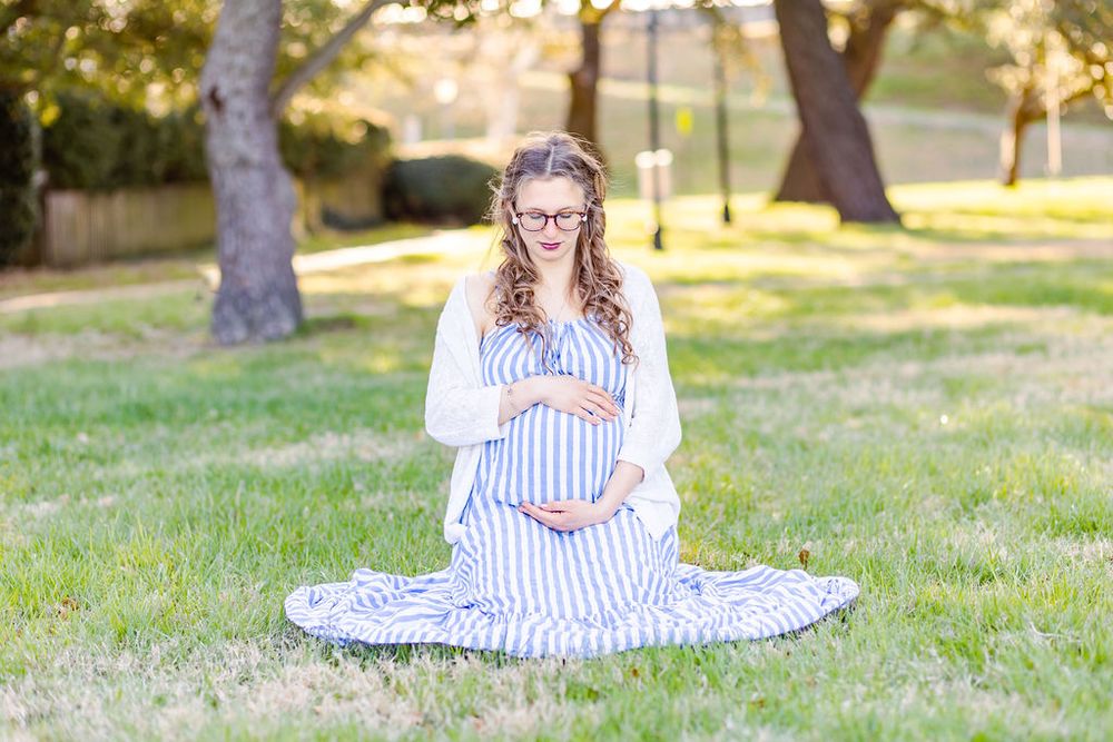Maternity photo in park setting with striped dress and spring greenery.