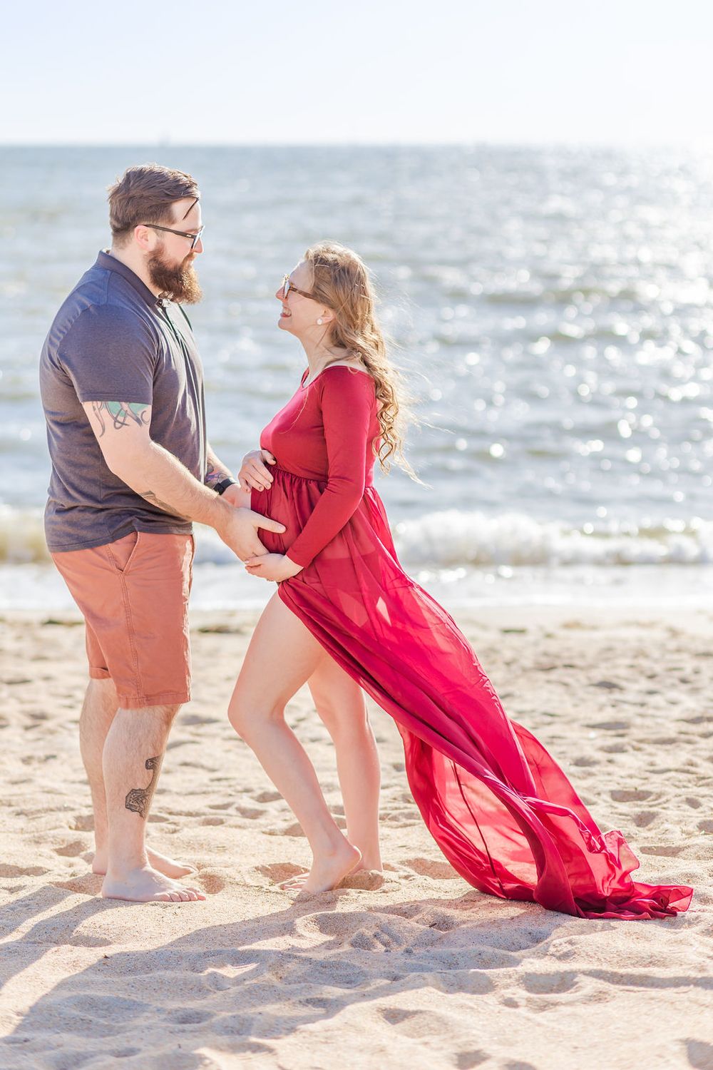 Romantic beach photoshoot with flowing red dress against sparkling ocean backdrop.