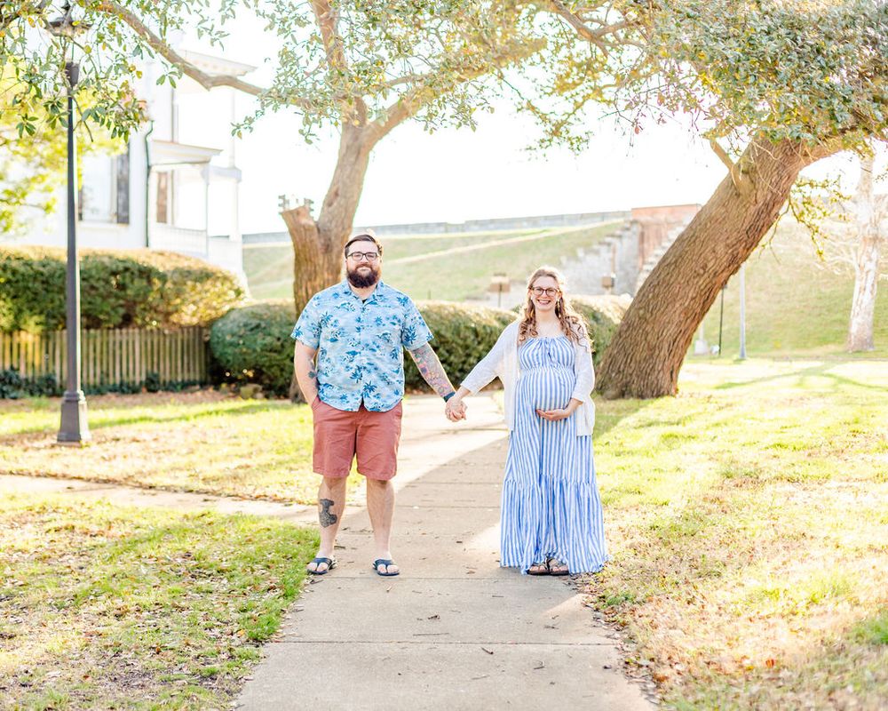 A maternity photoshoot on a pathway with a house and trees in the background.