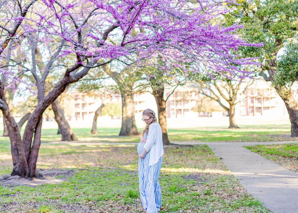 Person in light blue outfit standing under blooming purple spring trees.