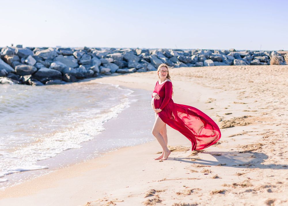 Figure in flowing red dress walking along beach near rocky jetty.