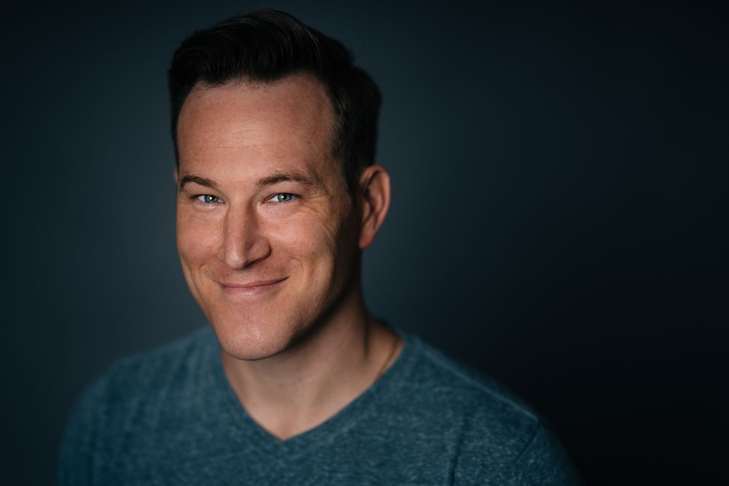 Portrait of a person in a teal shirt smiling against a dark blue background.