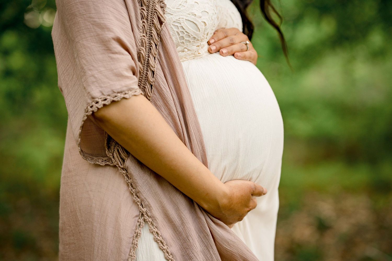 Close-up detail of cream maternity dress with lace overlay and mauve cardigan.
