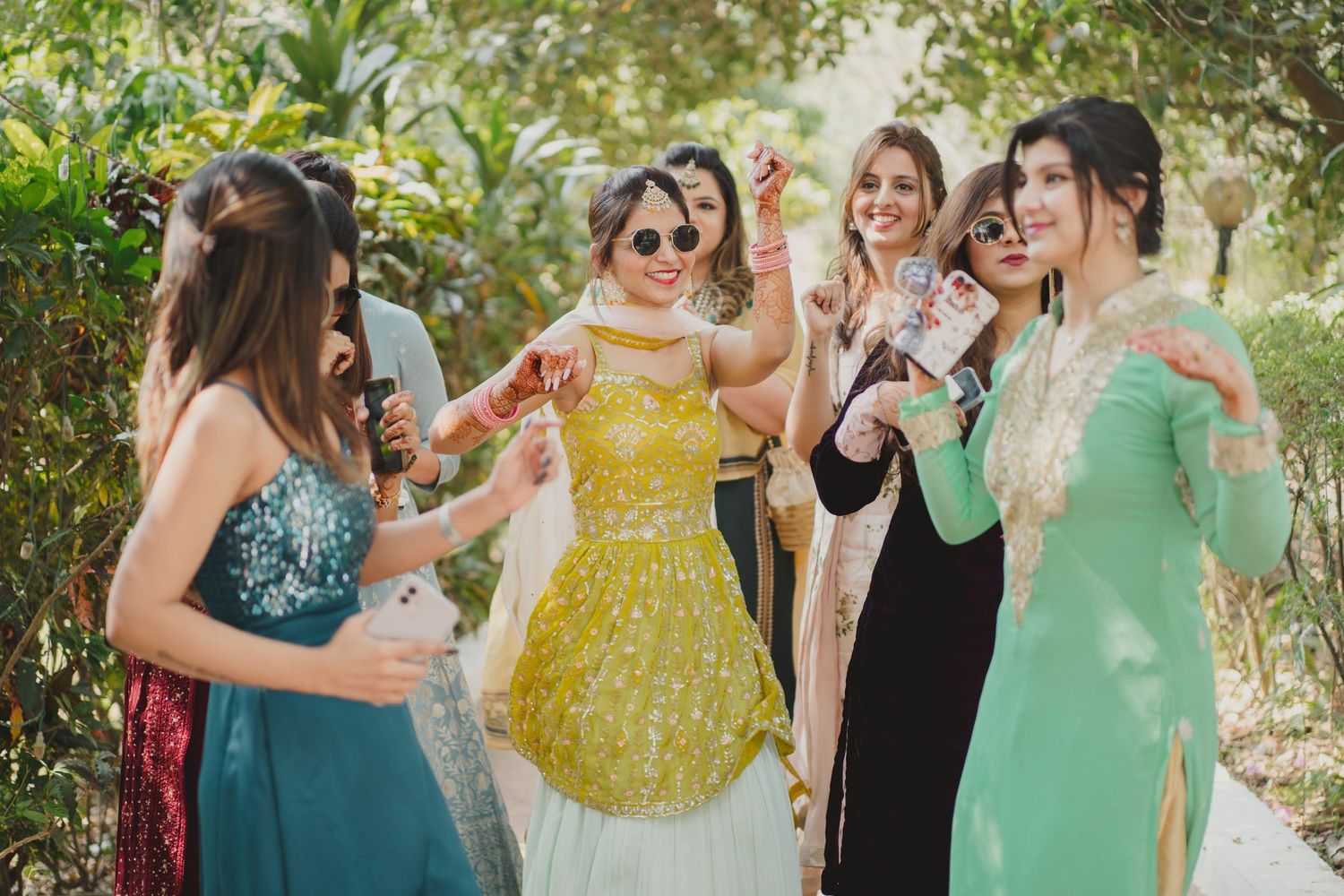 Wedding party in colorful dresses celebrating outdoors under trees.