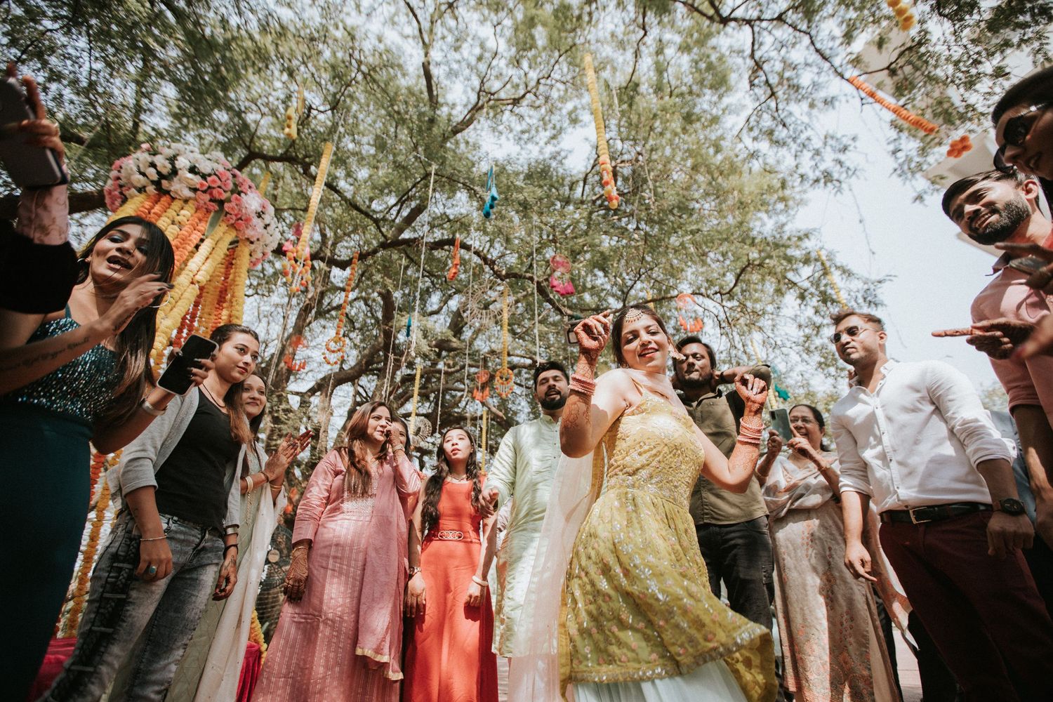 Joyful celebration scene with guests gathered outdoors under tree canopy.