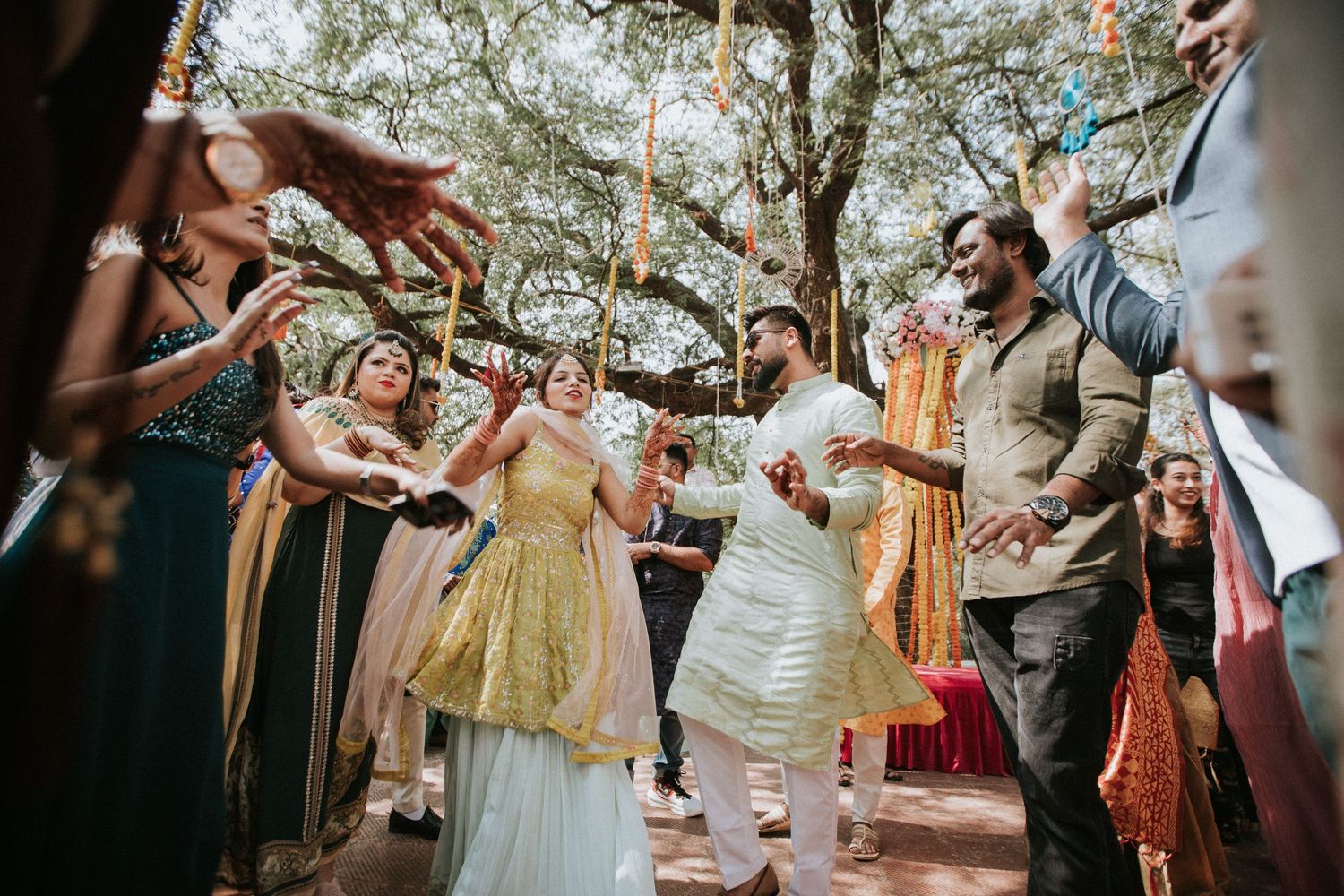 Festive outdoor celebration with orange marigold garlands hanging under trees during a cultural ceremony.