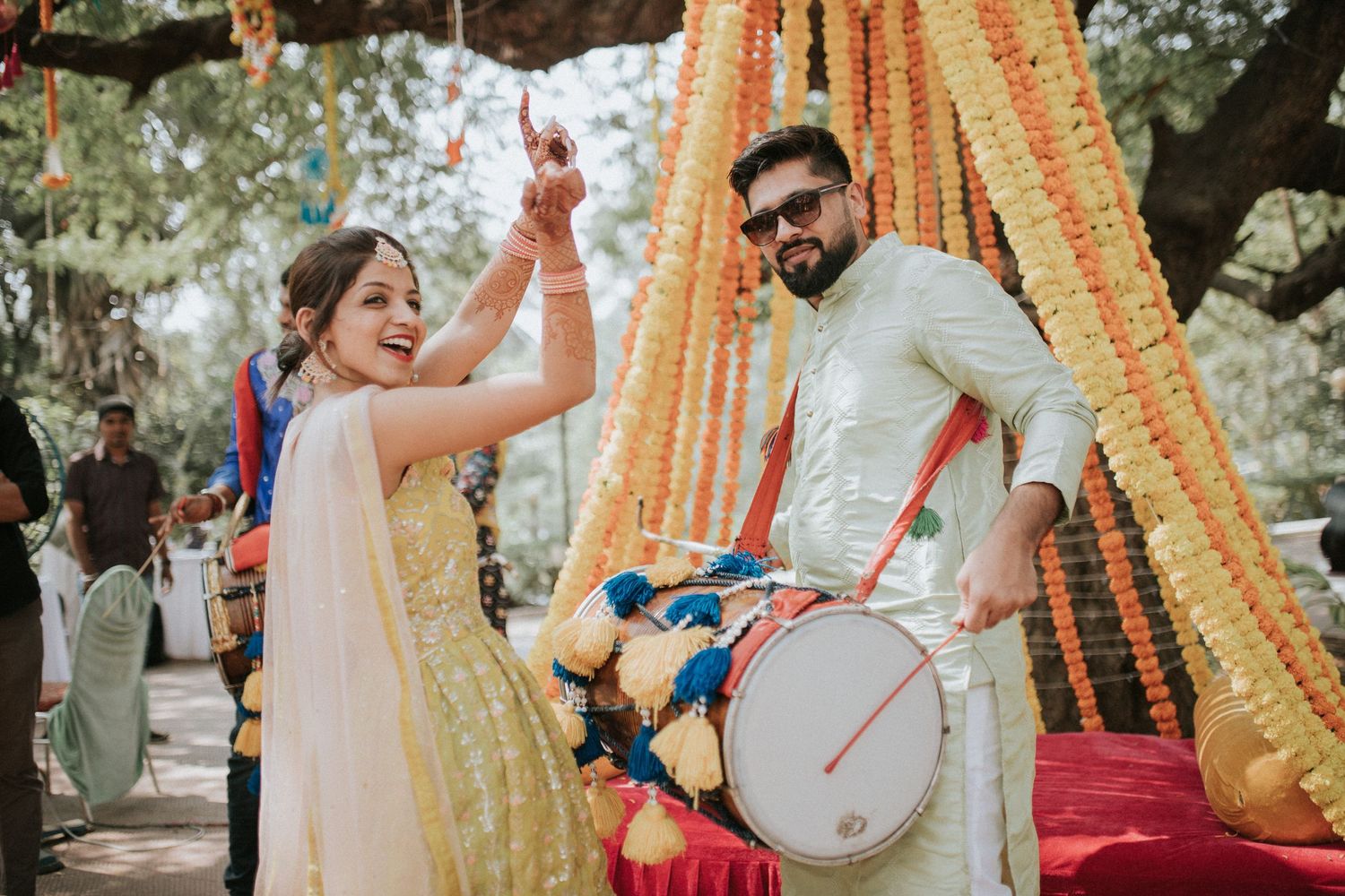 Outdoor celebration with traditional music and dancing against a backdrop of orange floral decorations.