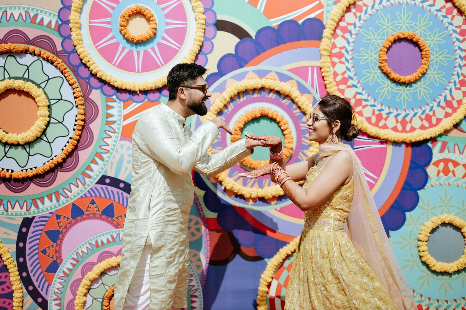 Dancing and celebration in front of a colorful geometric patterned backdrop at an Indian event.