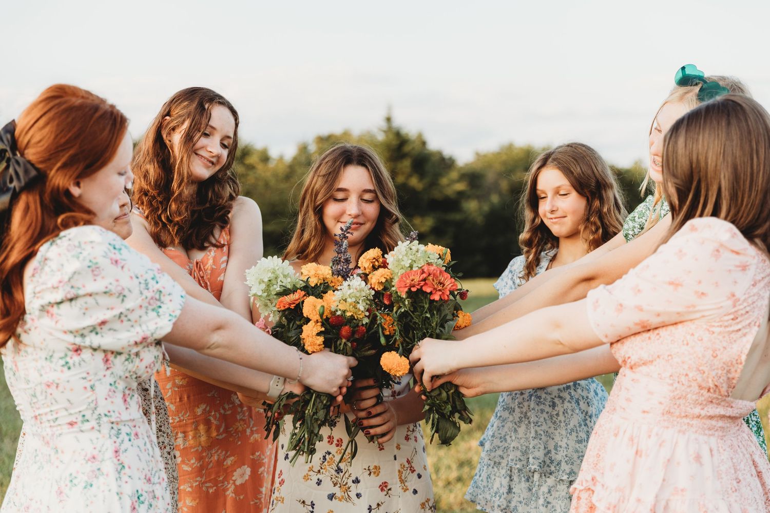 Group of women in floral dresses posing together outdoors at sunset.