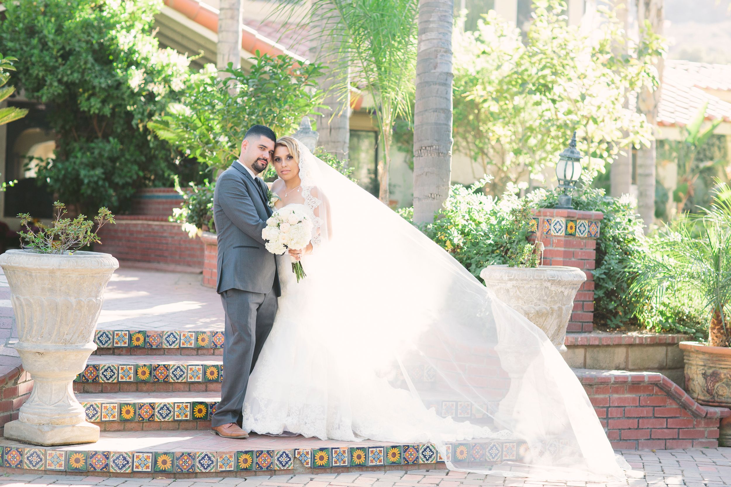 Wedding couple shares intimate moments against a backdrop of palm trees and brick architecture.