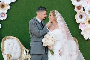 Wedding couple poses against green floral backdrop in elegant attire.