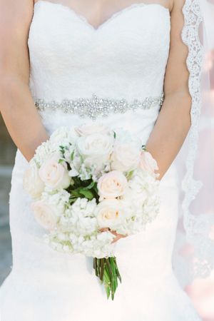 Close-up details of white wedding dress and cream rose bouquet with crystal embellishments.