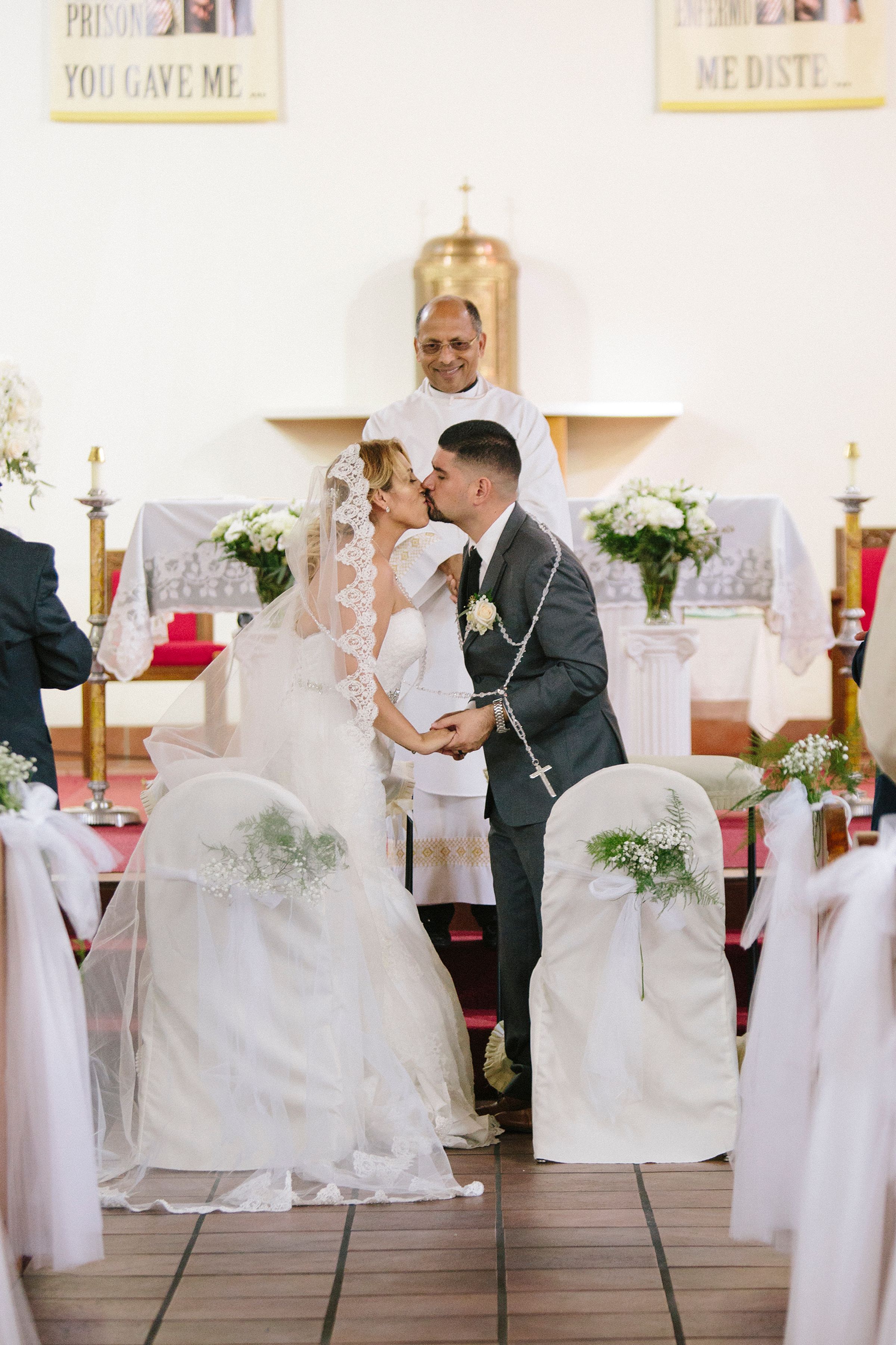 Church wedding ceremony with white floral decorations and draped chairs.