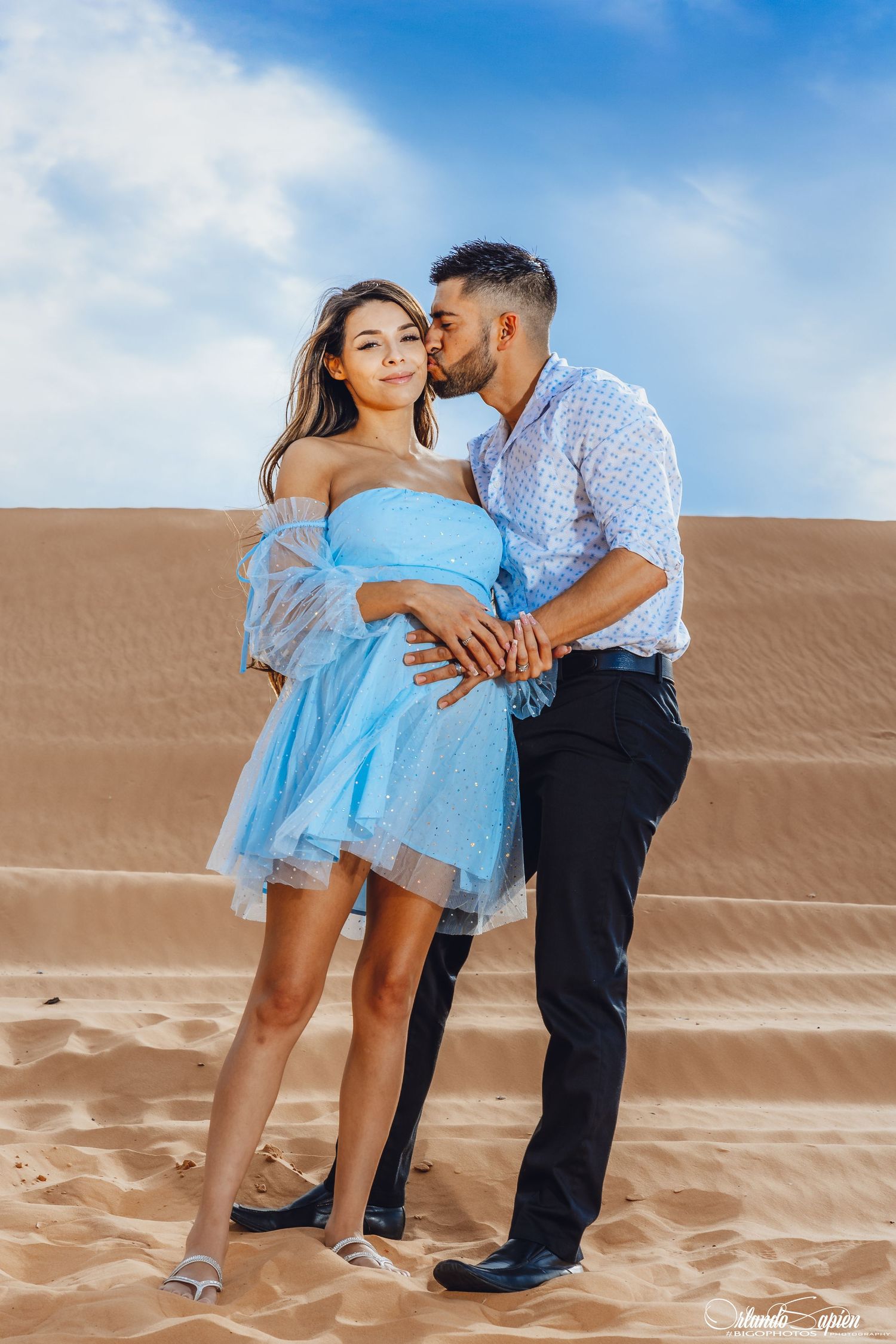 A romantic desert photo shoot featuring a couple in blue and white attire against sand dunes.