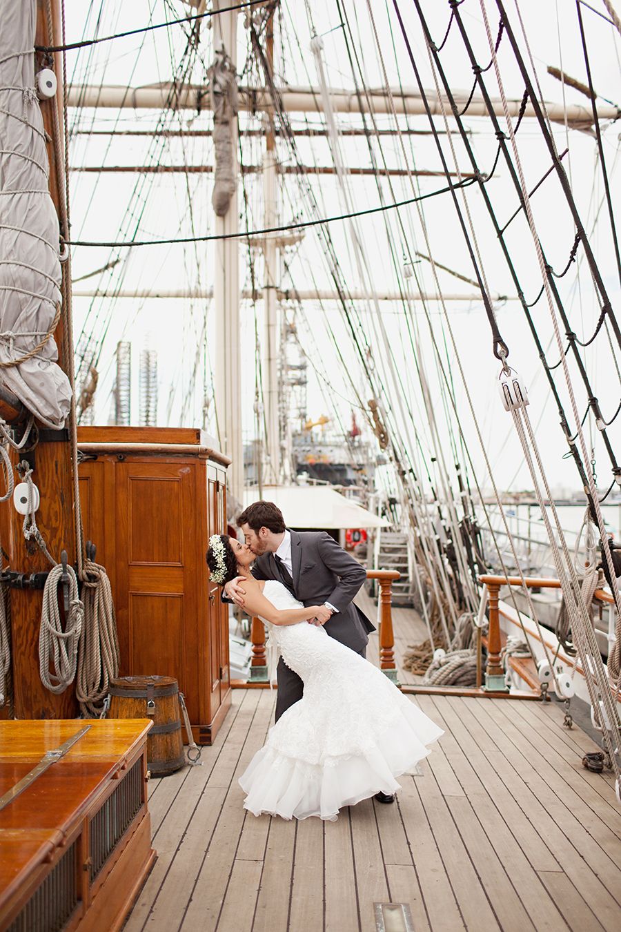 Wedding couple poses dramatically on the wooden deck of a historic sailing ship.
