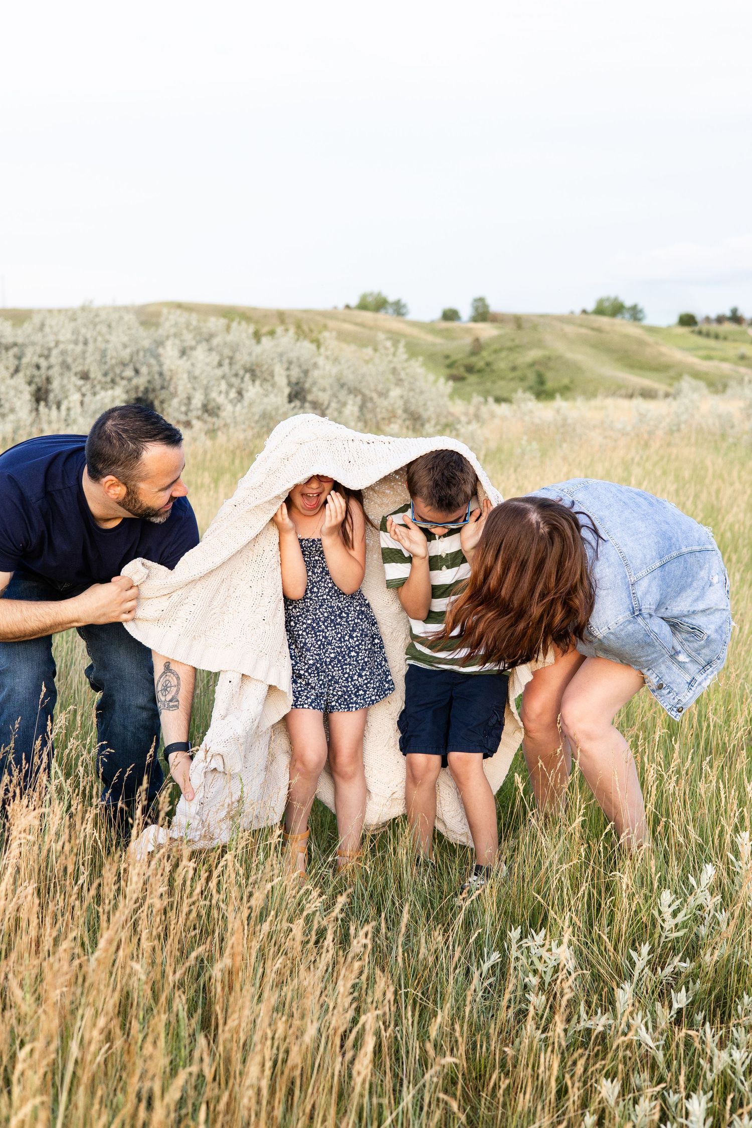 Family playing together under a blanket in a field of tall grass.
