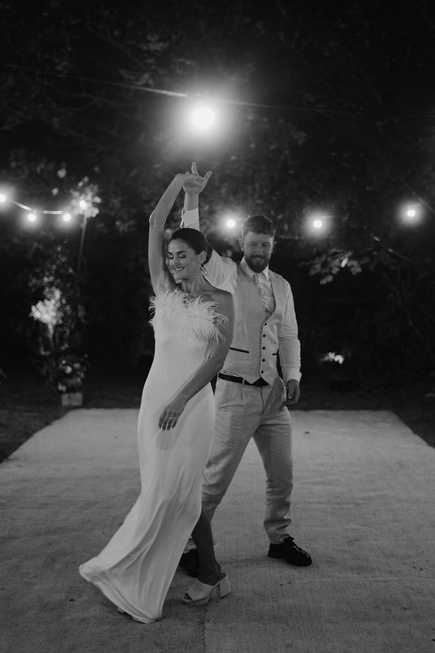 groom twirling bride surrounded by festoon lighting outside marquee in islip in oxfordshire