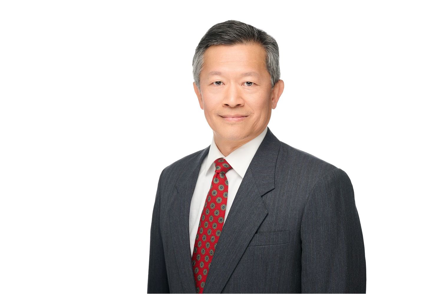 Business professional in dark suit and red tie photographed against white backdrop.
