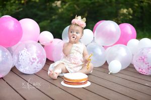 baby eating cake with hands in front of balloons