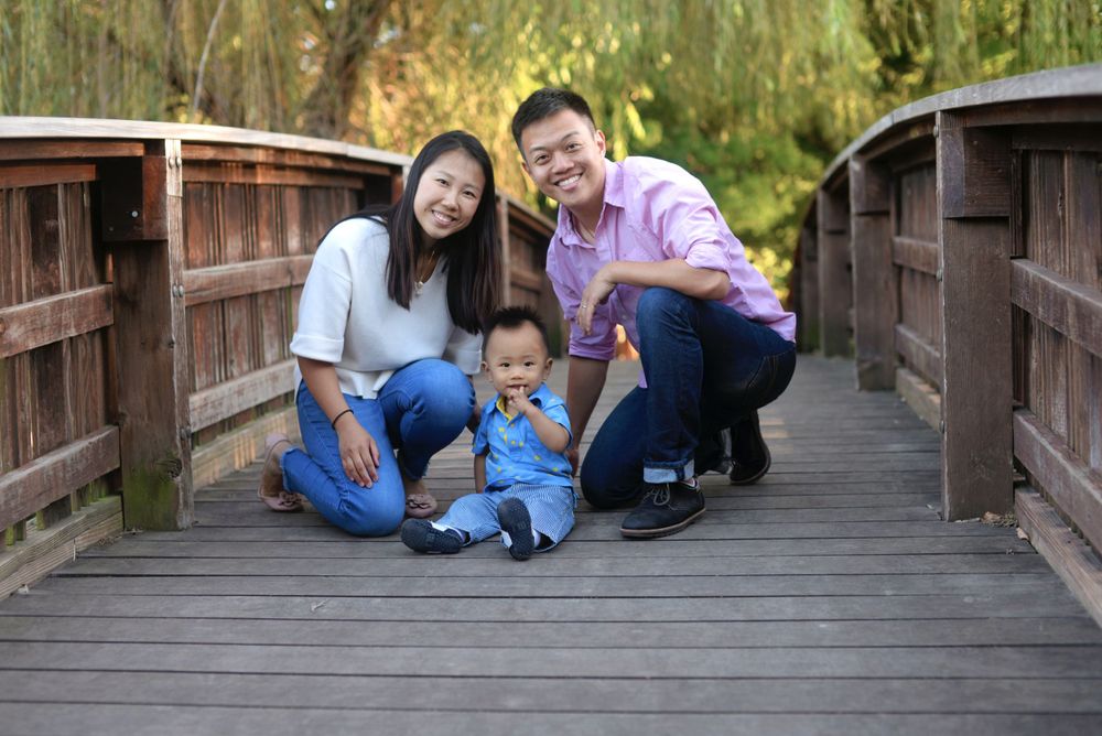 parents squatting together while baby sits between them on bridge