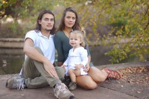 family of three sitting together in front of pond