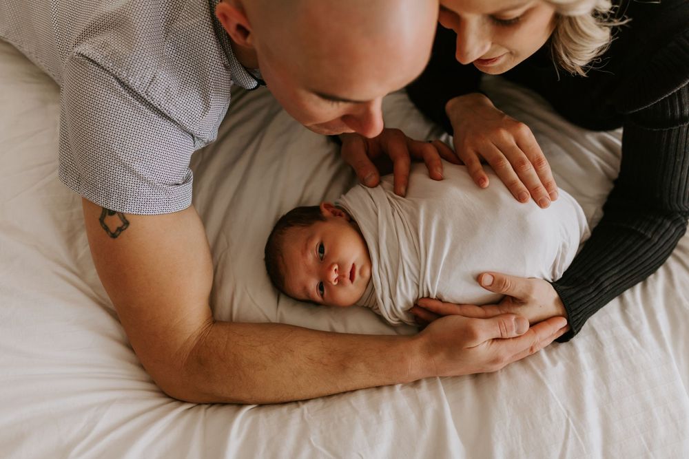 Loving family moment captured on white bedding in soft indoor lighting.