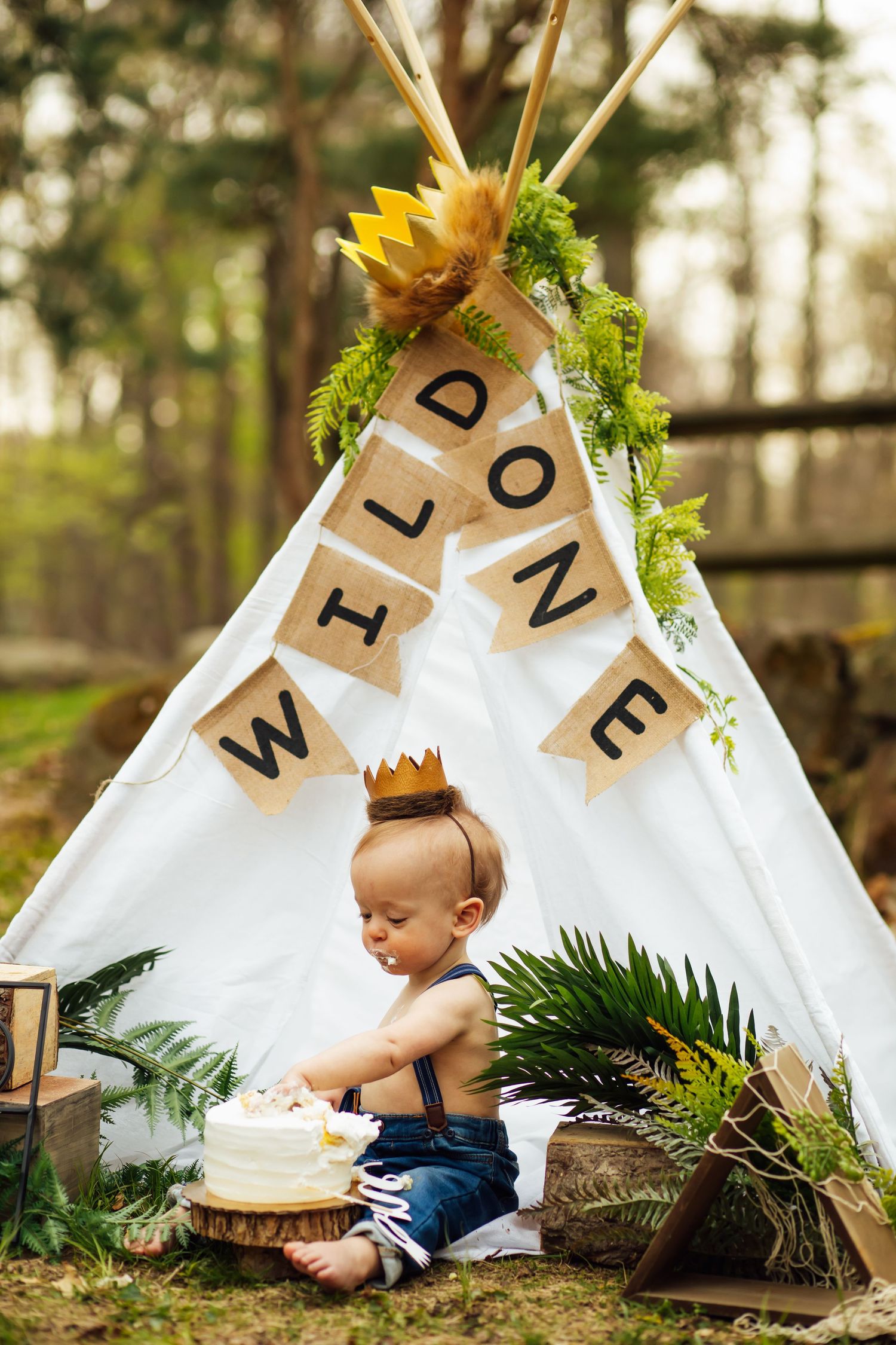 A small teepee decorated with letters and flowers serves as a backdrop for a cake smash photography setup.