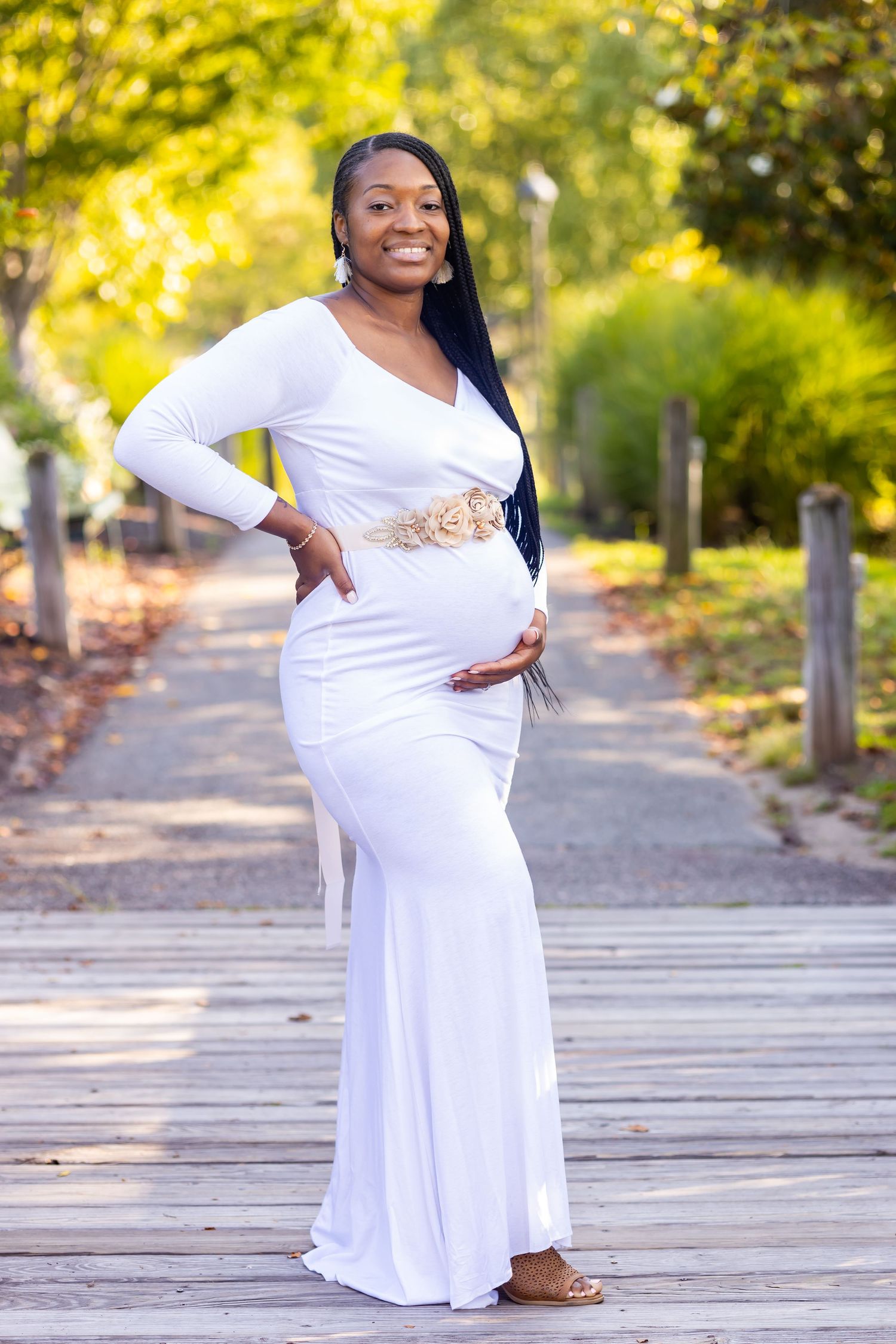 Beautiful maternity photo on wooden boardwalk with white dress and decorative sash in natural setting.