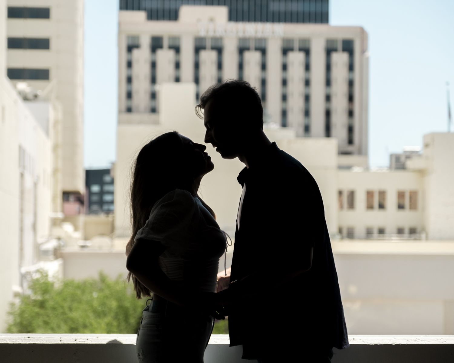 A romantic silhouette of a couple sharing an intimate moment against an urban city backdrop with buildings.