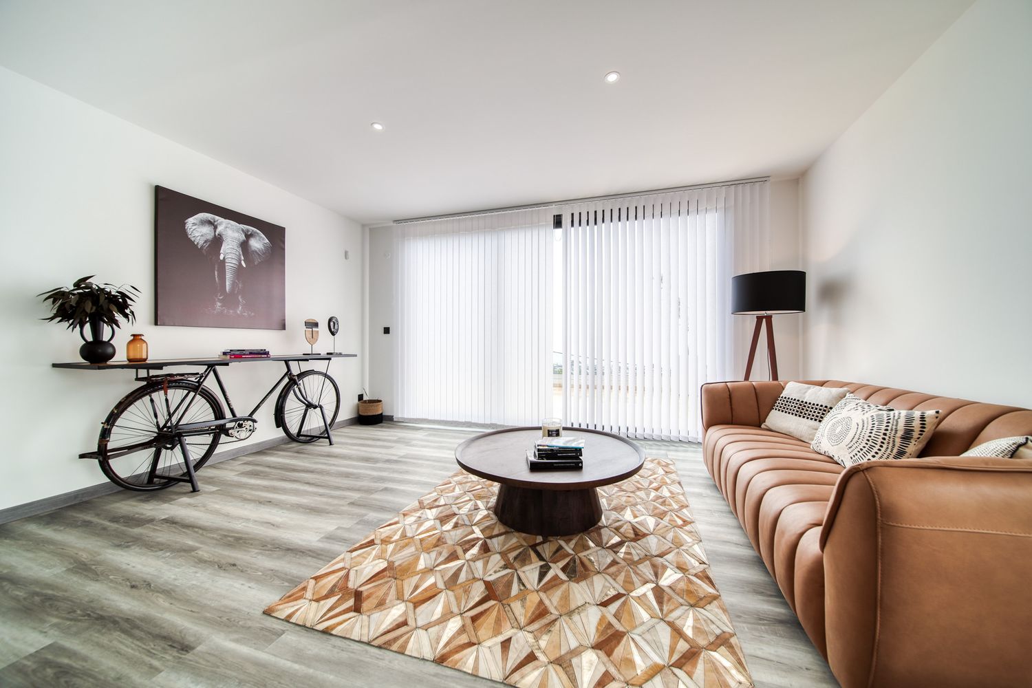Modern minimalist living room with tan leather sofa and artistic wooden sculptural installation on the floor.