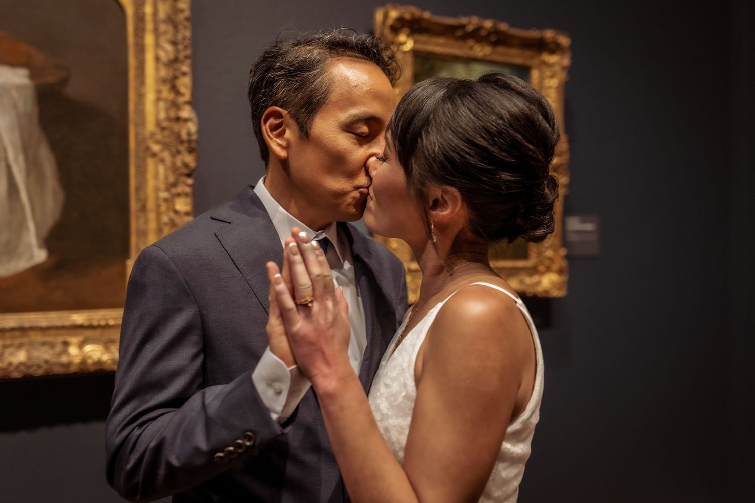 Romantic couple sharing an intimate moment in front of ornate gold-framed artwork in an art gallery.