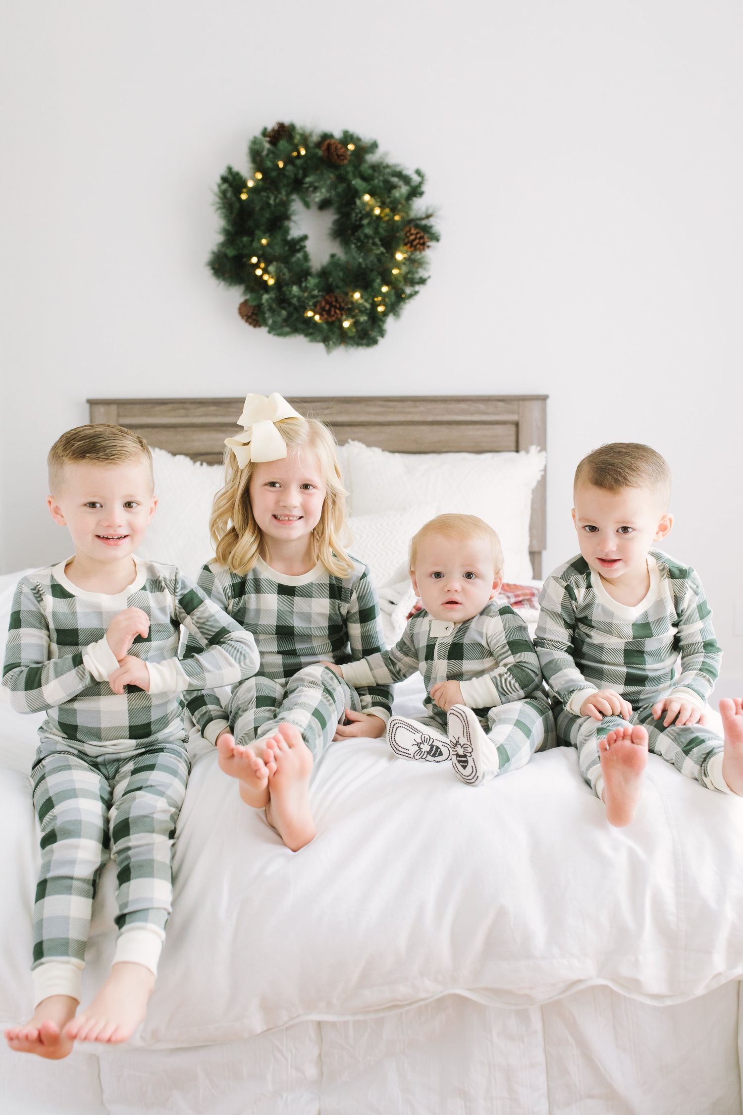 Group wearing matching plaid pajamas posing on white bed with holiday decorations.