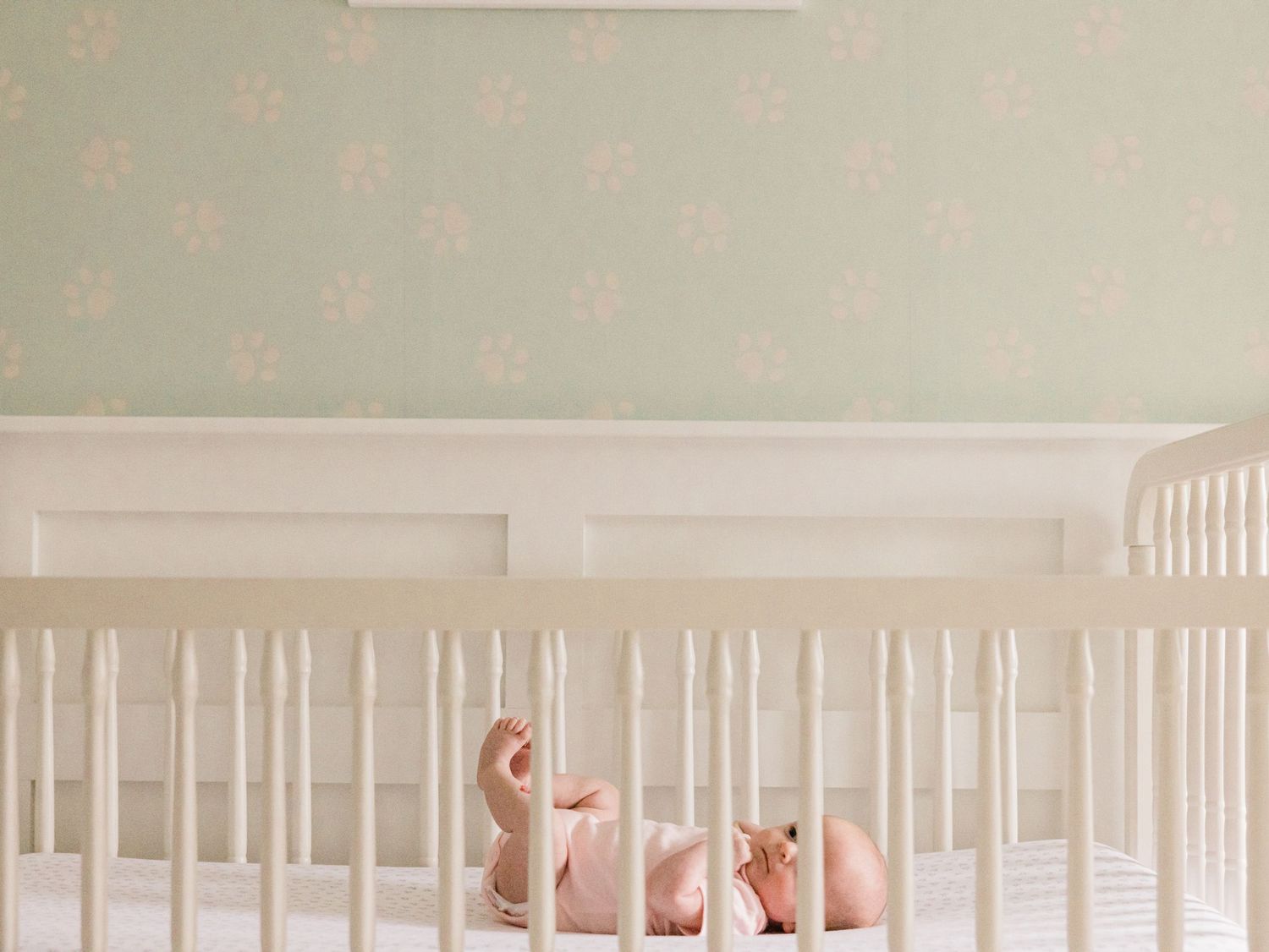 infant girl in crib pale green nursery