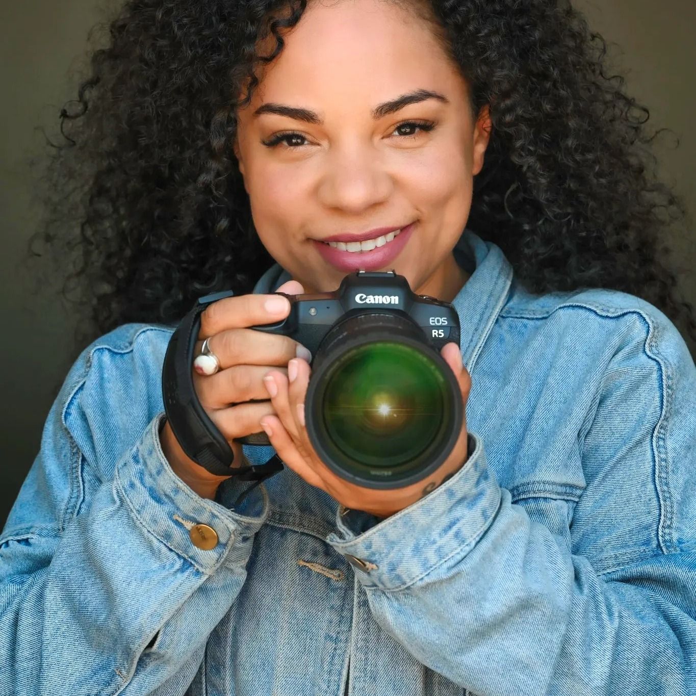 Photographer with curly hair in denim jacket taking photos with professional camera.