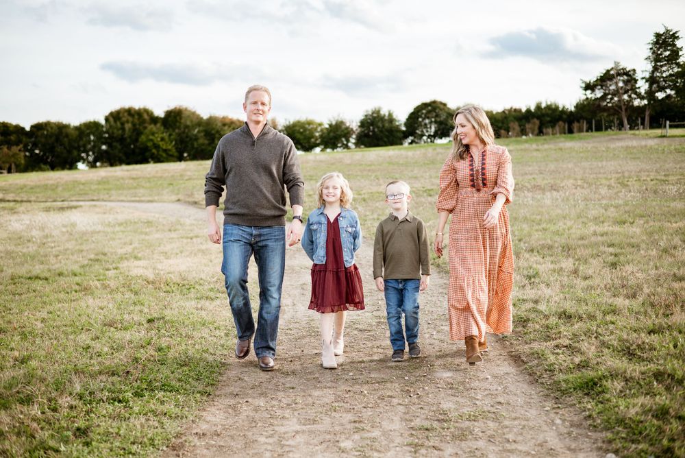 Family walking together across a pastoral field under cloudy skies.