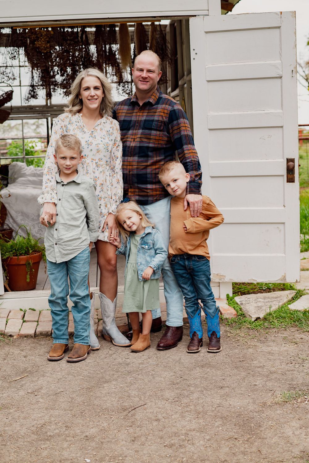 Family group standing together in casual clothes against white building exterior.
