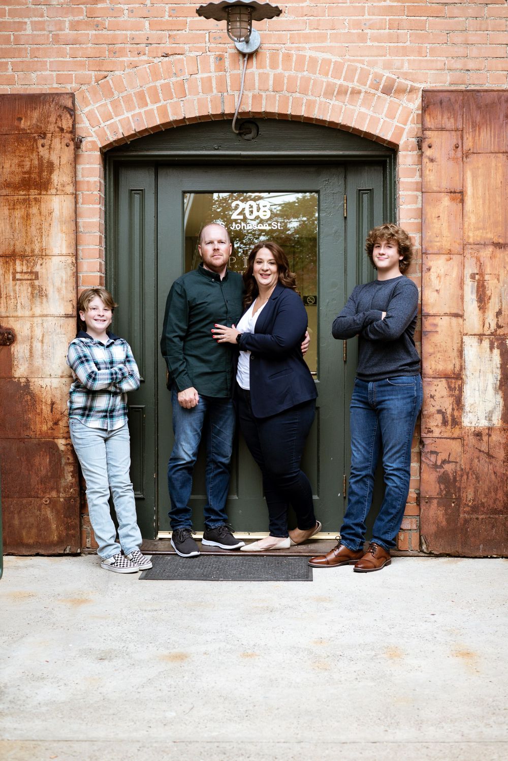 A series of casual poses in front of an industrial brick doorway with rusted metal door.