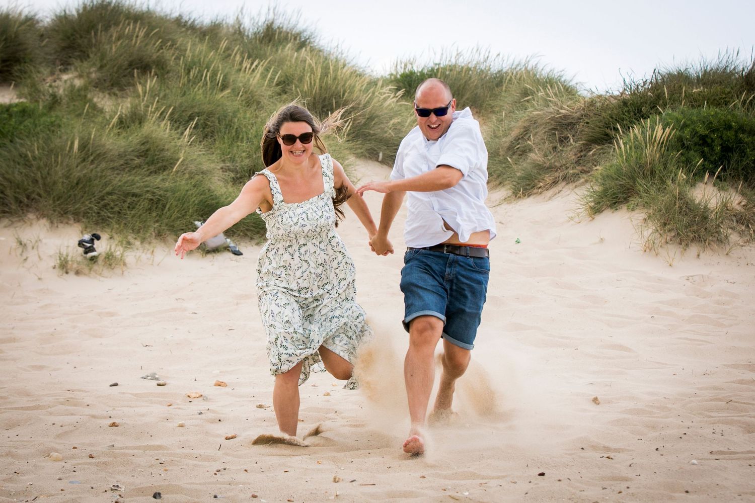 Playful couple running along sandy beach dunes on a summer day.
