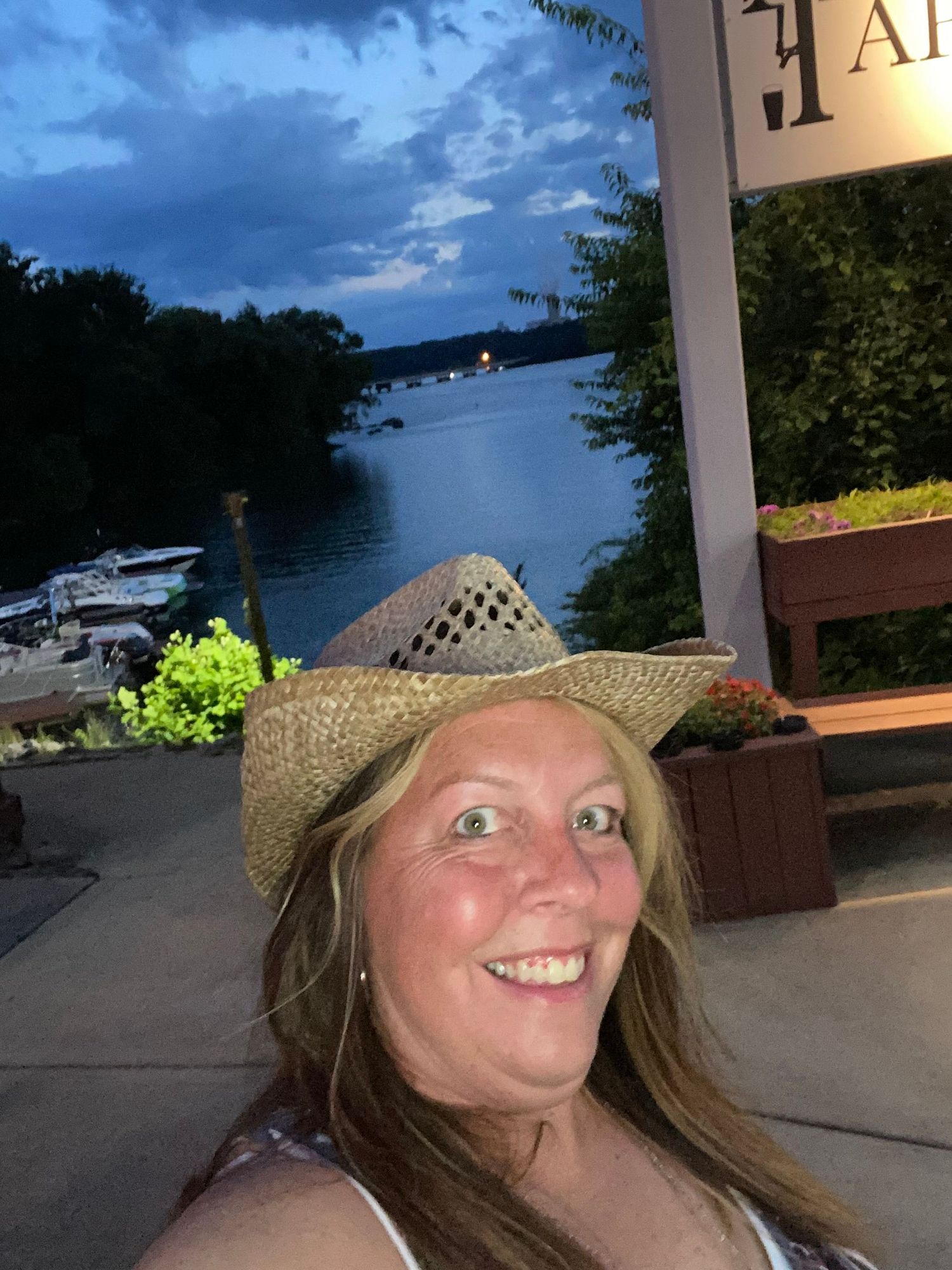 Woman in a straw hat taking selfies by a lake during sunset.