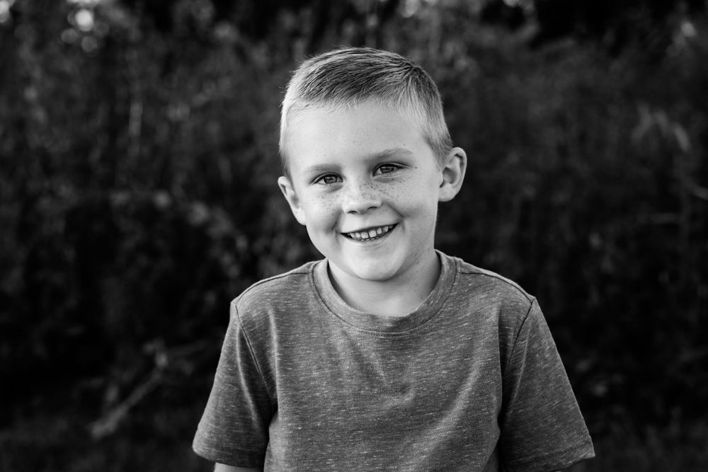 Happy young boy in a gray t-shirt smiles broadly in a black and white outdoor portrait.