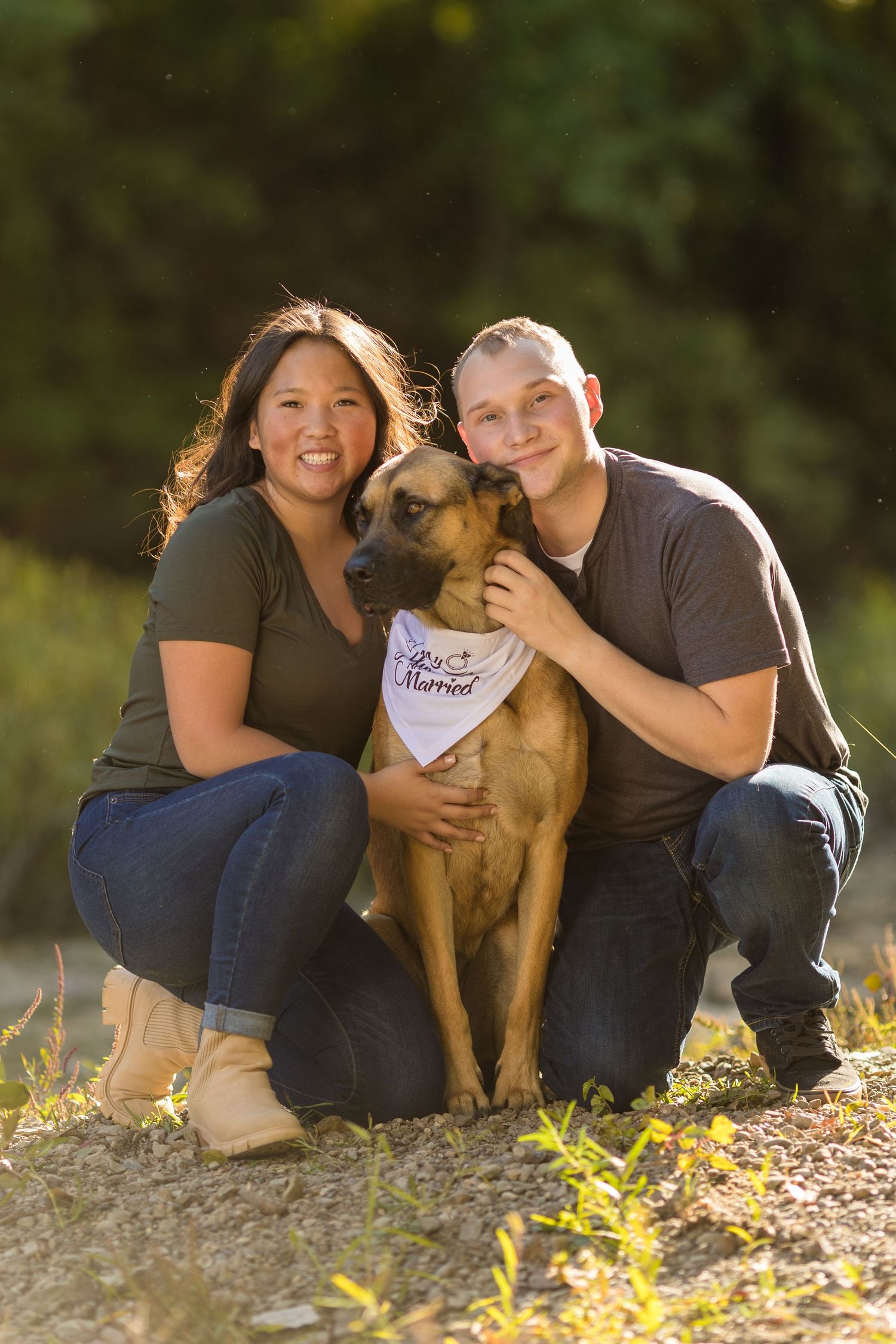 Young engaged couple pose with their dog, who is wearing a white bandana.