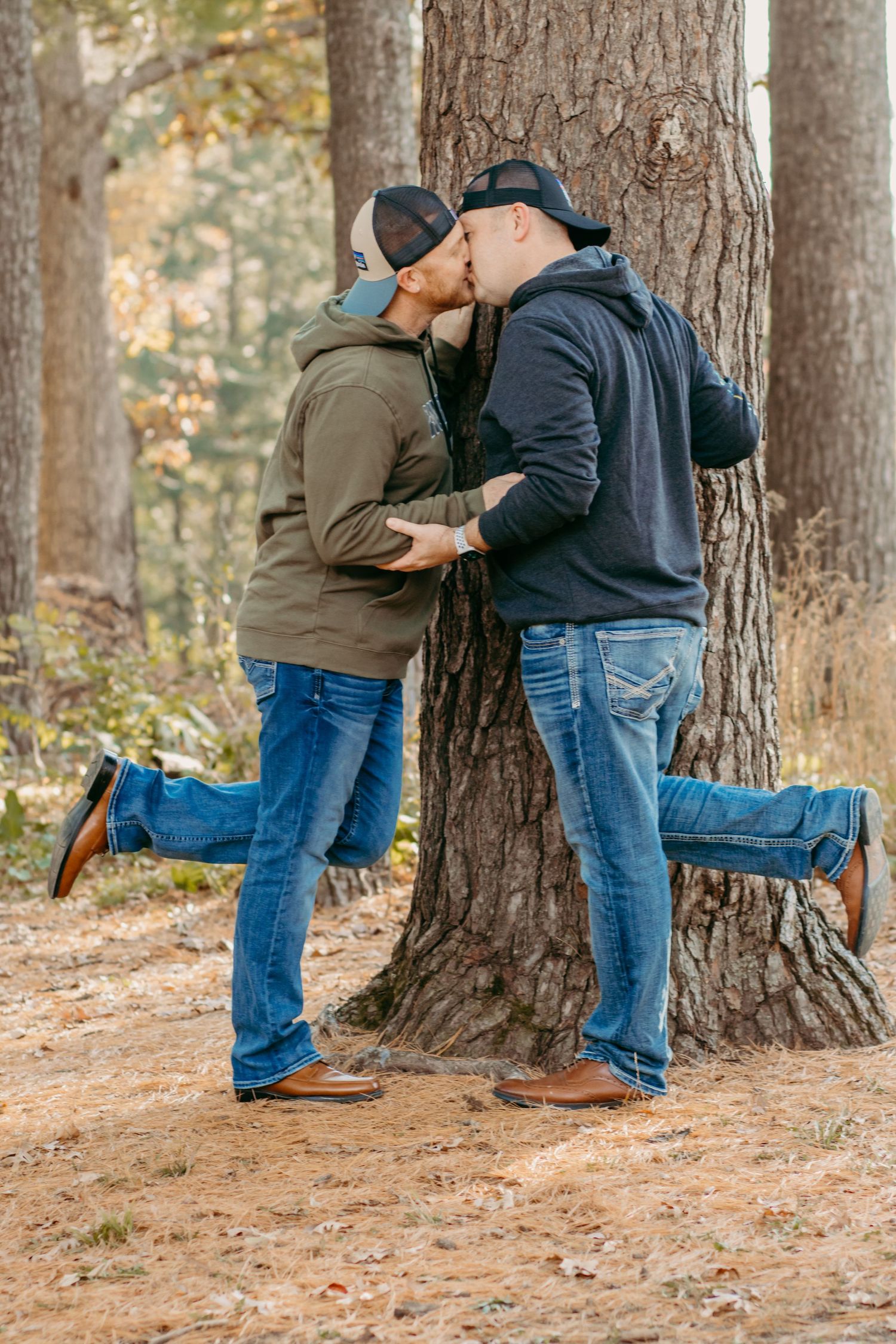 Couple embracing against large tree trunk in autumn forest setting.