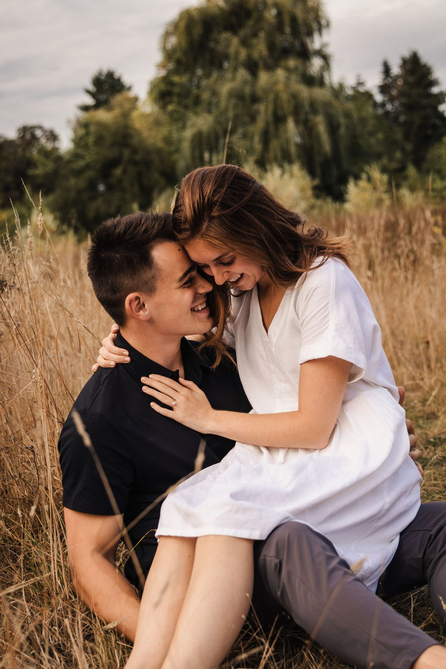 Couple sharing an intimate moment together in a golden wheat field with a willow tree in the background.