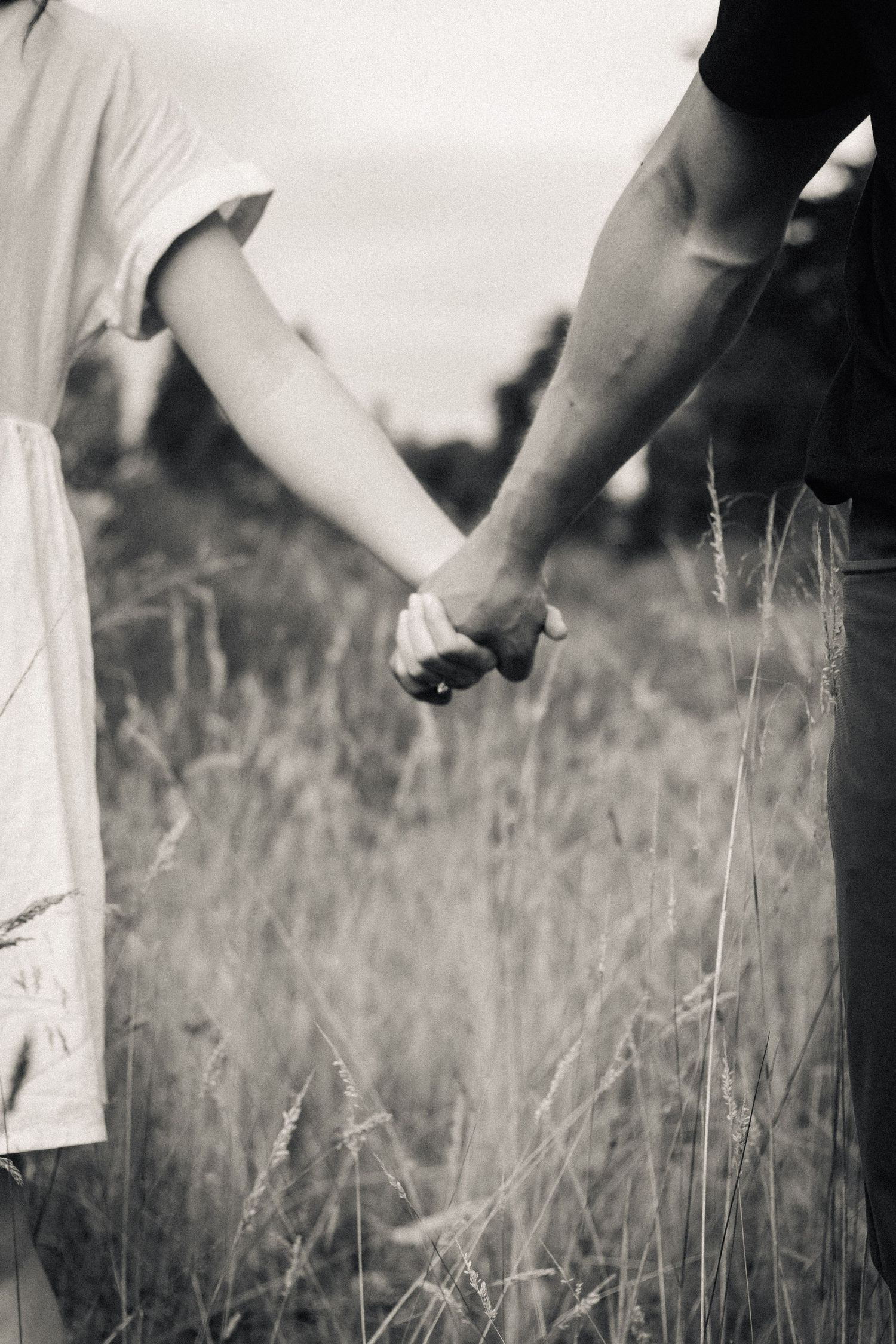 Black and white close-up of a couple holding hands in a field of tall grass.