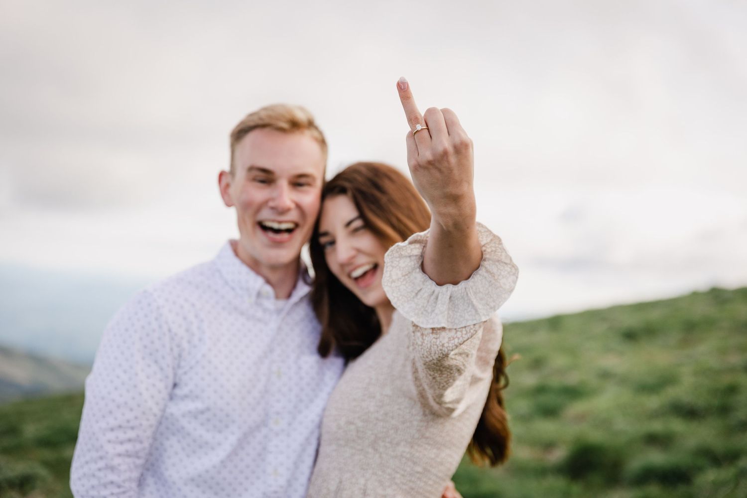 Happy couple sharing a joyful moment on a hilltop with mountains in the background.