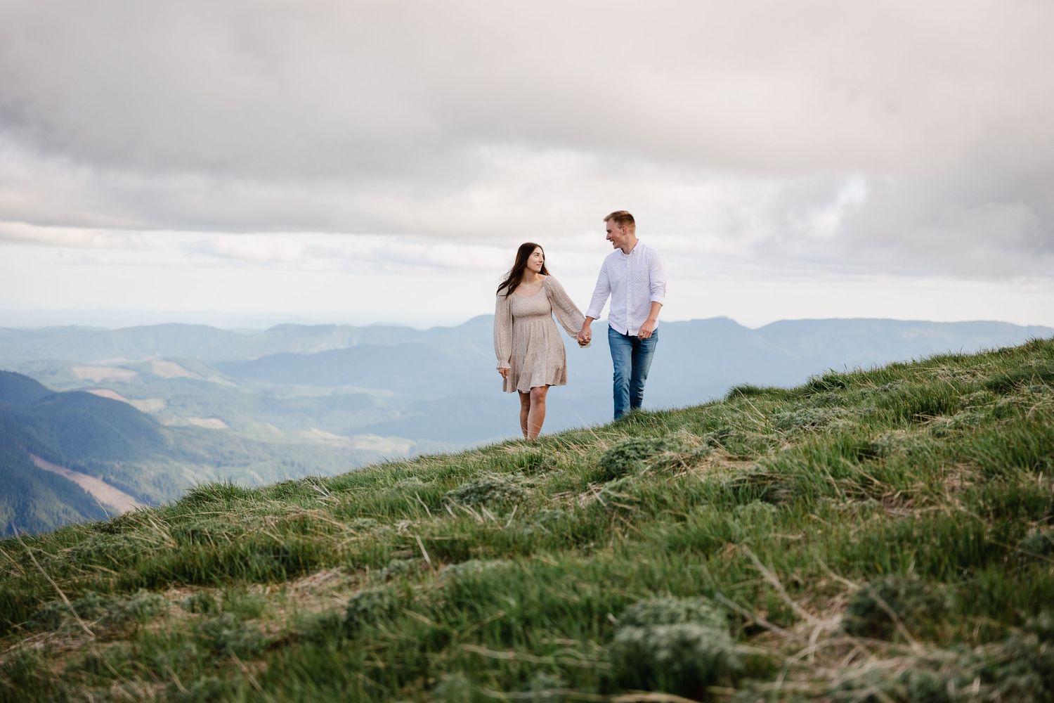 Couple walking along a mountain ridge with panoramic valley views below.