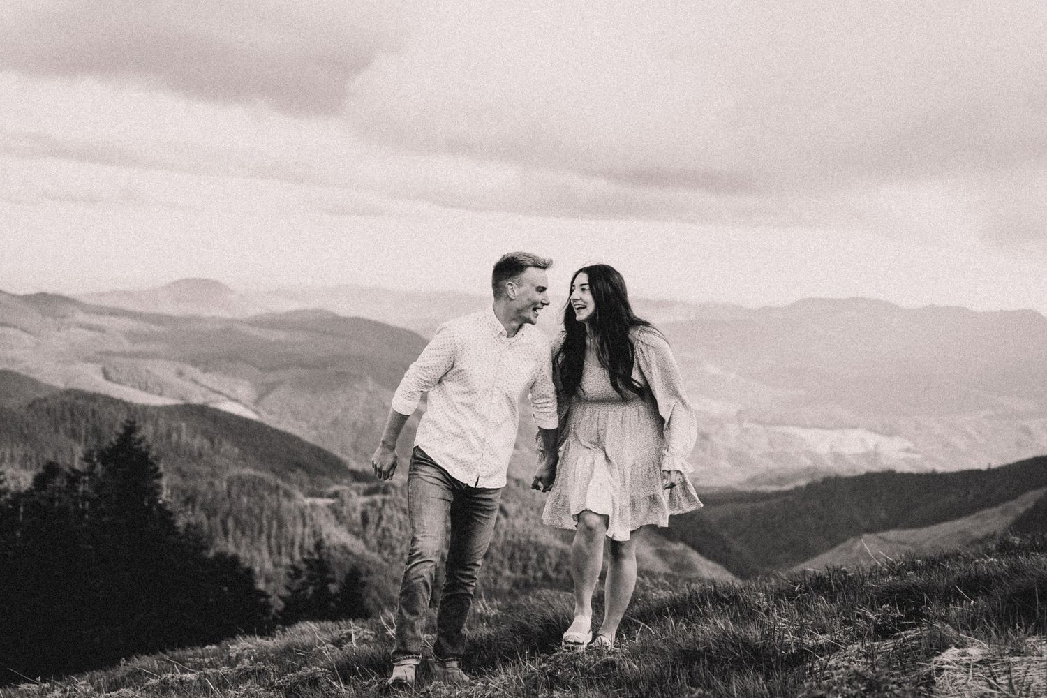 Couple walking together on a mountaintop with scenic valley views in black and white.